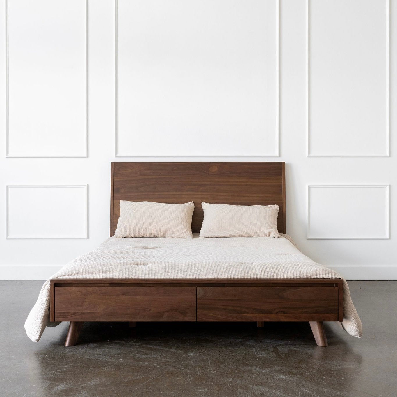 Walnut bed with white bedding against a white paneled wall